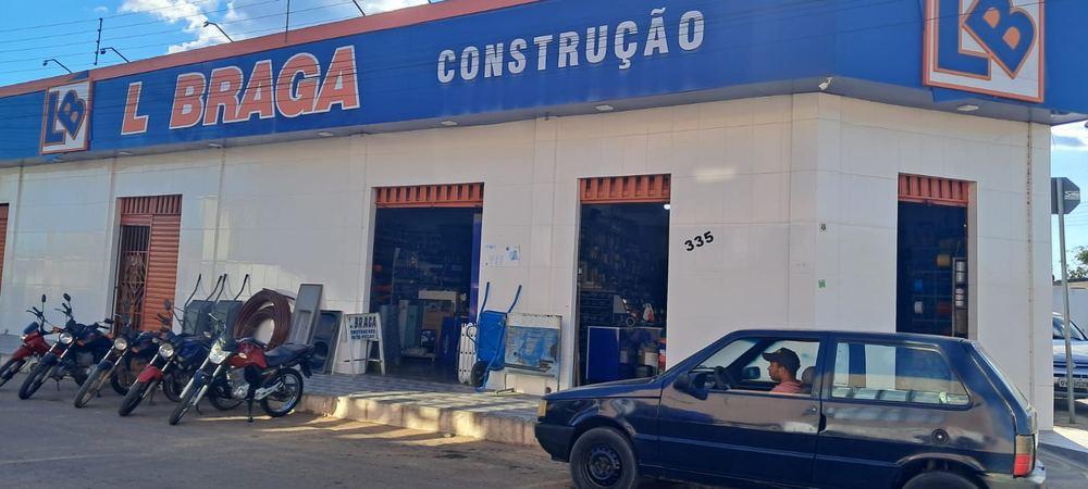 Fachada da loja do Centro: prédio branco com faixa azul e letreiro laranja L BRAGA CONSTRUÇÃO